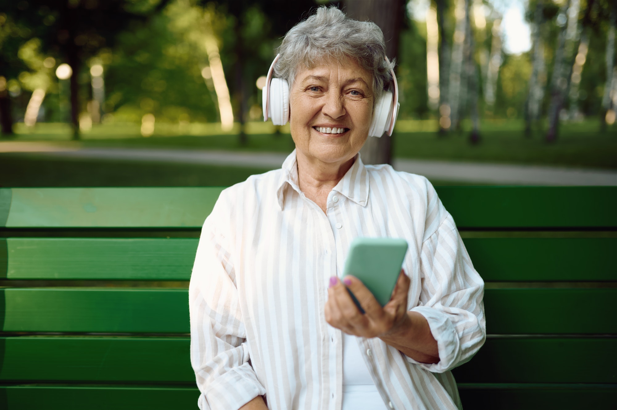 Old woman in headphones listens to music on bench