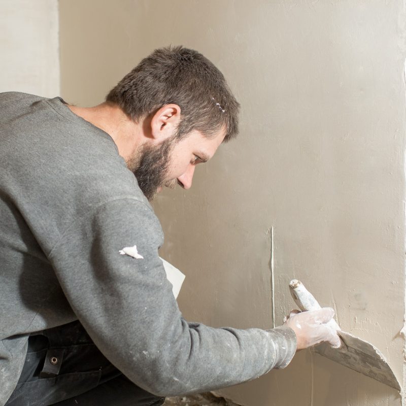 a male plasterer plasters a concrete wall with a spatula.