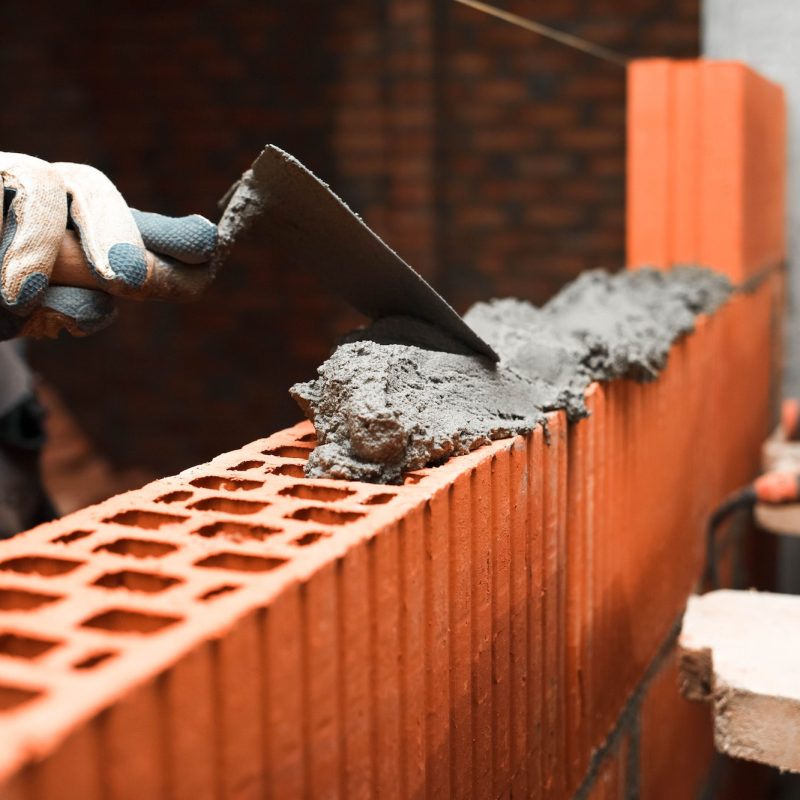 Bricklayer puts bricks to make a wall