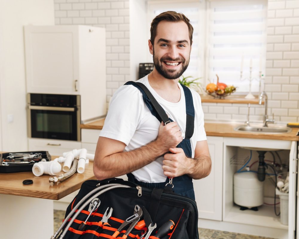 Image of plumber man smiling and holding bag with equipment in apartment